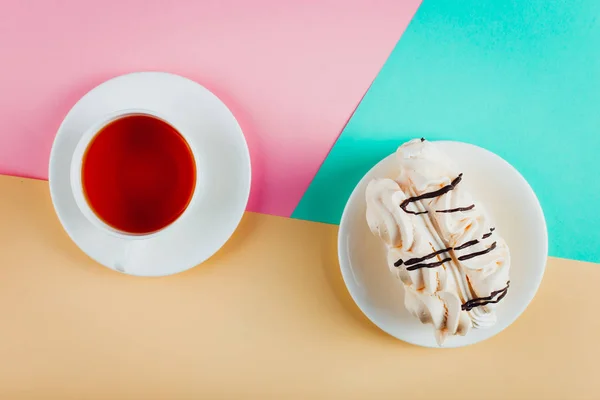 Maräng tårta på ett tefat och en kopp te på pastell färgade papper bakgrund. — Stockfoto