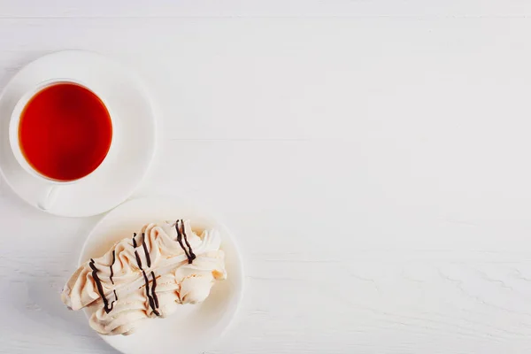 Кексик с безе и чашка чая на белом деревянном столе . — стоковое фото