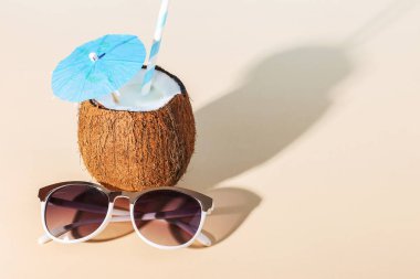 Tropikal kokteyl bardağı taşıran damla, bir şemsiye, güneş gözlüğü, kabuk Sarı zemin üzerine Hindistan cevizi. Gevşeme, yaz ruh hali, kopya alanı kavramı.