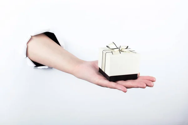 Weibliche Hand aus einem Loch in Papier, hält ein kleines Geschenk. isolieren auf weißem Hintergrund. — Stockfoto