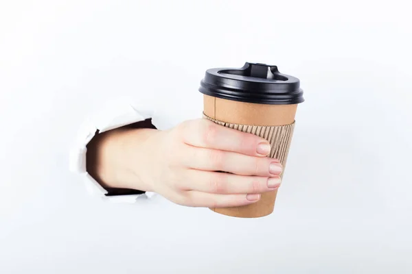 Vrouwelijke hand uit het gat in de paperman, houdt een bruinglas koffie met hem. Isoleren op witte achtergrond. — Stockfoto