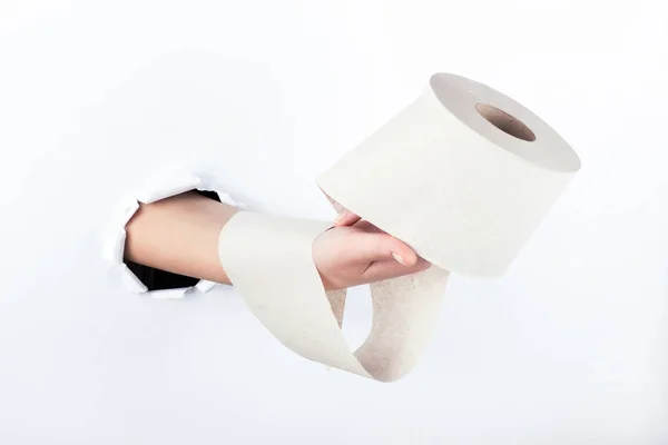 Mano femenina fuera del agujero en el papelero, sosteniendo un rollo de papel higiénico. Aislar sobre fondo blanco . — Foto de Stock