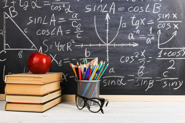 School desk in classroom, with books on background of chalk board with written formulas. Soncept Teacher\'s Day.