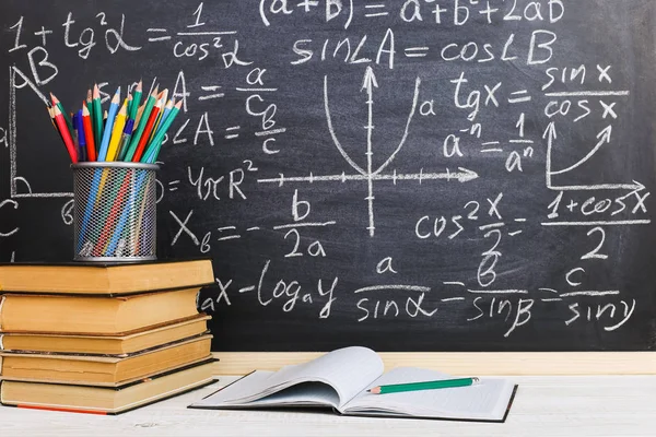 Schulbank im Klassenzimmer, mit Büchern auf dem Hintergrund einer Kreidetafel mit geschriebenen Formeln. Soncept Lehrertag. — Stockfoto