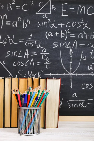 School desk in classroom, with books on background of chalk board with written formulas. Soncept Teacher\'s Day.