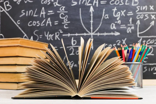 Mesa da escola em sala de aula, com livros sobre fundo de giz com fórmulas escritas. Soncept Dia do Professor . — Fotografia de Stock