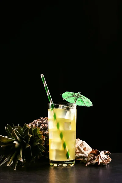 Cocktail all'ananas con tubo di ghiaccio e ombrello su fondo nero. Frutta tropicale e conchiglie, umore estivo in uno stile scuro . — Foto Stock