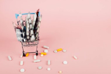Alışveriş sepeti hapları pembe bir arka plan üzerinde yüklü. İlaç ve uyuşturucu satışı kavramı. Kopya alanı.