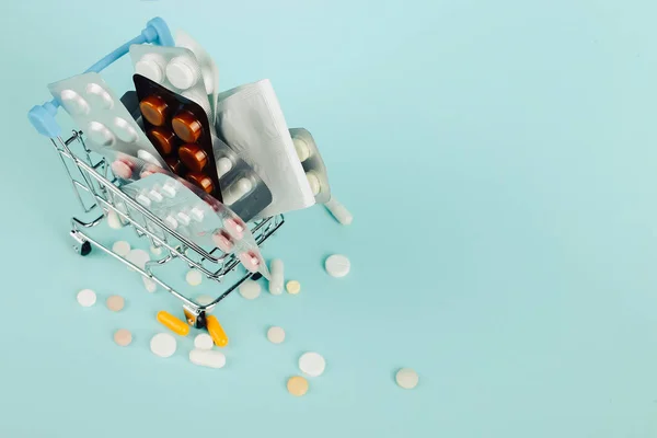 Καλάθι αγορών φορτωμένο με χάπια σε μπλε φόντο. Η έννοια της ιατρικής και την πώληση των ναρκωτικών. Χώρο αντίγραφο. — Φωτογραφία Αρχείου