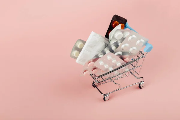 Kundvagn laddad med piller på en rosa bakgrund. Begreppet medicin och försäljning av narkotika. Kopiera utrymme. — Stockfoto