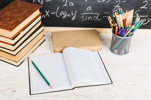 Escritorio escolar en aula, con libros sobre fondo de pizarra con fórmulas escritas. Día del Maestro Soncept . — Foto de Stock