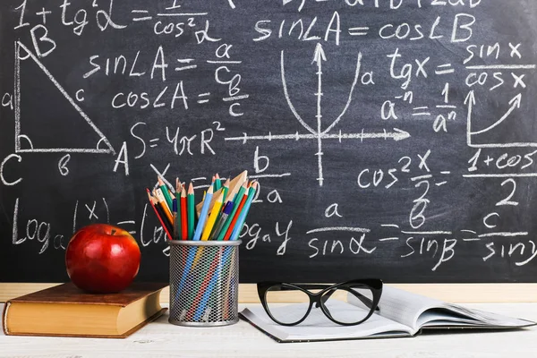 School desk in classroom, with books on background of chalk board with written formulas. Soncept Teacher\'s Day.