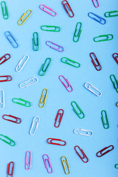 Multicolored paper clips on a blue background, pattern, copy space.