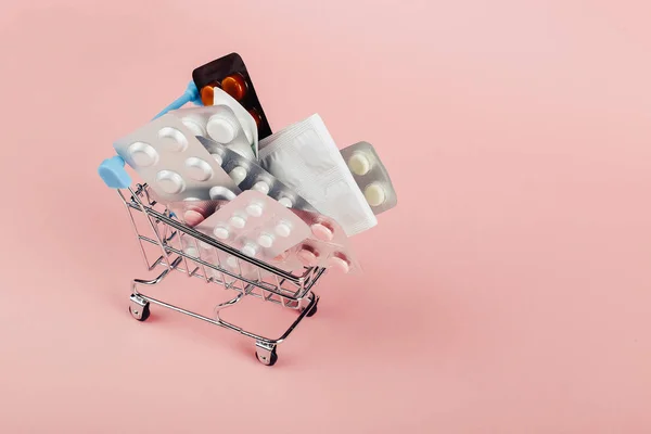 Kundvagn laddad med piller på en rosa bakgrund. Begreppet medicin och försäljning av narkotika. Kopiera utrymme. — Stockfoto