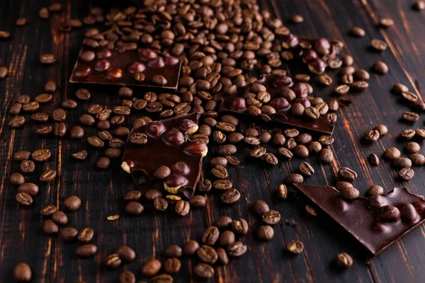 Scattered coffee grains and black chocolate on a wooden table.