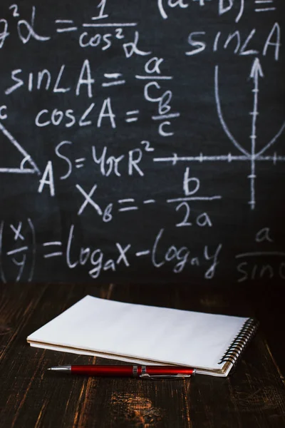 School desk in classroom, with books on background of chalk board with written formulas. Soncept Teacher\'s Day.