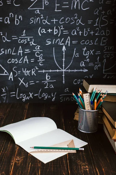 Mesa da escola em sala de aula, com livros sobre fundo de giz com fórmulas escritas. Soncept Dia do Professor . — Fotografia de Stock