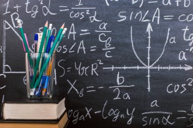 Kitaplar ve formüller ile bir tebeşir tahtası arka plan karşı, ahşap bir masa üzerinde kalem standı. Öğretmenler günü kavramı ve okula geri.