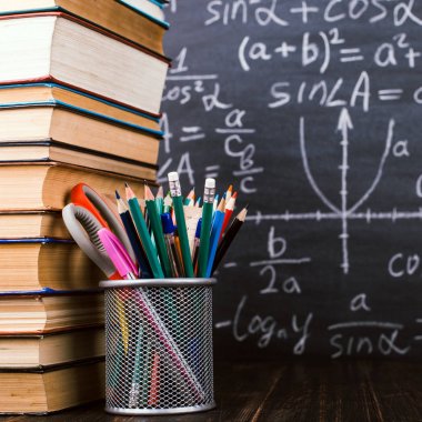 Kitaplar ve formüller ile bir tebeşir tahtası arka plan karşı, ahşap bir masa üzerinde kalem standı. Öğretmenler günü kavramı ve okula geri.