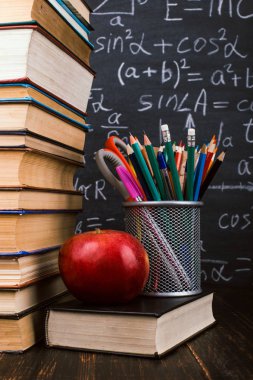 Kitaplar, bir elma, formüller ile tebeşir tahtası arka plan karşı, ahşap masa üzerinde kalem standı. Öğretmenler günü kavramı ve okula geri.