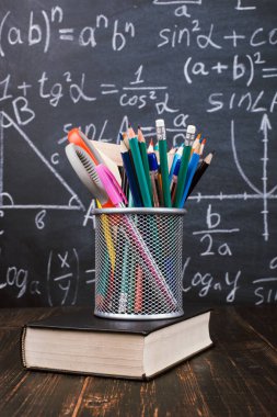 Kitaplar ve formüller ile bir tebeşir tahtası arka plan karşı, ahşap bir masa üzerinde kalem standı. Öğretmenler günü kavramı ve okula geri.