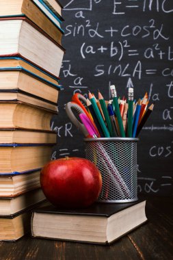 Kitaplar, bir elma, formüller ile tebeşir tahtası arka plan karşı, ahşap masa üzerinde kalem standı. Öğretmenler günü kavramı ve okula geri.