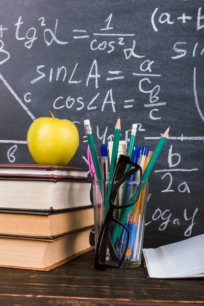 Ноутбук, очки, яблоко и стакан с карандашами на фоне доски с формулами. Концепция Дня учителя и возвращение в школу . — стоковое фото