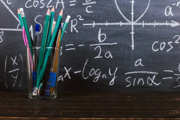 Очки и стакан с карандашами на фоне доски с формулами. Концепция Дня учителя и возвращение в школу . — стоковое фото