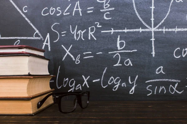 Книги на деревянном столе, на фоне меловой доски с формулами. Концепция Дня учителя и возвращение в школу . — стоковое фото