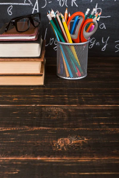 Libros y soportes para bolígrafos sobre una mesa de madera, sobre el fondo de una pizarra de tiza con fórmulas. Concepto del día del maestro y de vuelta a la escuela . — Foto de Stock