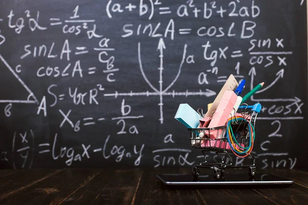 A shopping cart with school supplies on tablet, on table against background chalkboard. Concept back to school preparation and online shopping.