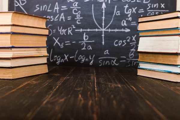 Formülleri ile bir tebeşir tahtası arka plan karşı ahşap bir masa üzerinde Kitaplar. Öğretmenler günü kavramı ve okula geri.