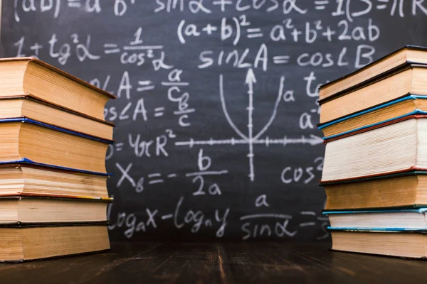 Boeken op een houten tafel, tegen de achtergrond van een krijtbord met formules. Teacher's Day concept en terug naar school. — Stockfoto