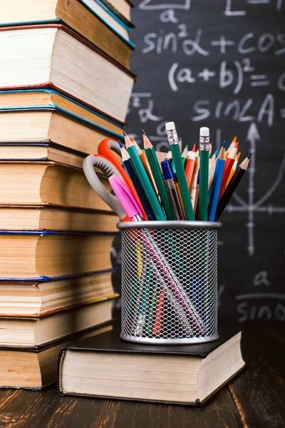 Книги и стенд для ручек на деревянном столе, на фоне меловой доски с формулами. Концепция Дня учителя и возвращение в школу . — стоковое фото