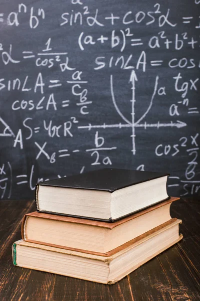 Formülleri ile bir tebeşir tahtası arka plan karşı ahşap bir masa üzerinde Kitaplar. Öğretmenler günü kavramı ve okula geri.