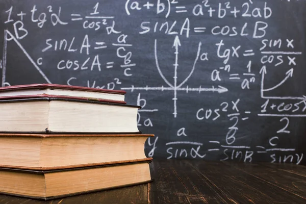 Formülleri ile bir tebeşir tahtası arka plan karşı ahşap bir masa üzerinde Kitaplar. Öğretmenler günü kavramı ve okula geri.