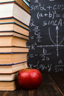 Kitaplar ve tahta bir masa üzerinde bir elma, formülleri ile bir tebeşir tahtası arka plan karşı. Öğretmenler günü kavramı ve okula geri.