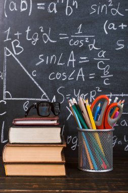 Kitaplar ve formüller ile bir tebeşir tahtası arka plan karşı, ahşap bir masa üzerinde kalem standı. Öğretmenler günü kavramı ve okula geri.