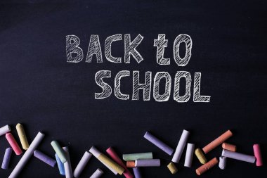 Çok renkli boya kalemleri siyah bir tebeşir tahtası üzerinde yatıyor, kopya alanı. Okul, eğitim ve çocukluk kavramı.