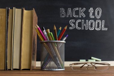 Gözlük öğretmen kitapları ve tebeşir ile bir tahta arka plan üzerinde, masada kalem ile bir stand. Öğretmenler günü kavramı. Kopyalama alanı.