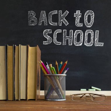 Gözlük öğretmen kitapları ve tebeşir ile bir tahta arka plan üzerinde, masada kalem ile bir stand. Öğretmenler günü kavramı. Kopyalama alanı.