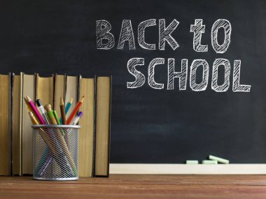 Ders kitapları ve okul malzemeleri bir masada, tebeşirle bir tahta arka plan karşı. Copyspase ile okul kavramı.