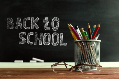 Gözlük öğretmen ve tebeşir ile bir tahta arka plan üzerinde, masada kalem ile bir stand. Öğretmenler günü kavramı. Kopyalama alanı.