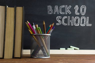 Ders kitapları ve okul malzemeleri bir masada, tebeşirle bir tahta arka plan karşı. Copyspase ile okul kavramı.