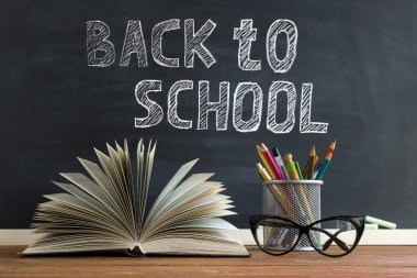 Gözlük öğretmen kitapları ve tebeşir ile bir tahta arka plan üzerinde, masada kalem ile bir stand. Öğretmenler günü kavramı. Kopyalama alanı.