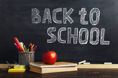 Yazma malzemeleri, bir kitap ve bir elma, metin için boş veya bir okul teması için bir arka plan ile Öğretmen masası. Kopyalama alanı.