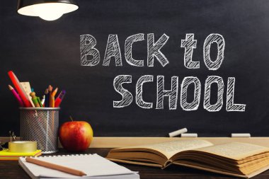 Öğretmenin masası ya da bir işçi, hangi yazı malzemeleri yalan, bir kitap ve bir elma, akşam lamba altında. Okul teması için metin veya arka plan için boş. Kopyalama alanı.