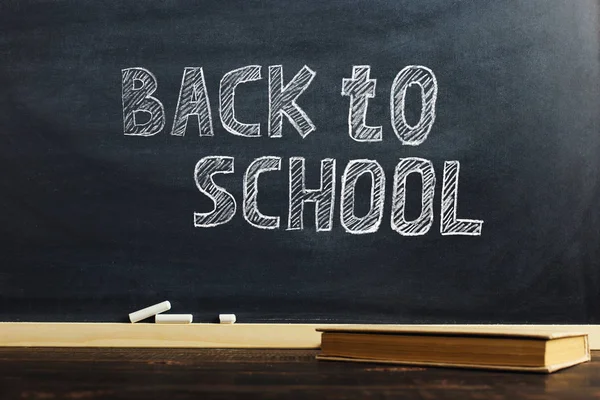 Black chalk board over wooden table with book, blank for text or background for school theme.