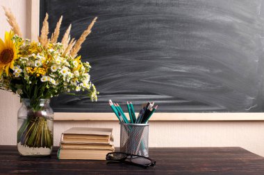 Gözlük öğretmen kitapları ve kır çiçekleri buket masada, tebeşir ile arka plan tahta üzerinde. Öğretmenler günü kavramı. Kopyalama alanı.