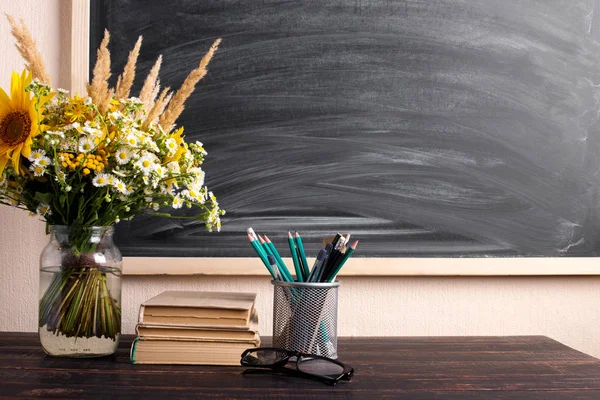 Gözlük öğretmen kitapları ve kır çiçekleri buket masada, tebeşir ile arka plan tahta üzerinde. Öğretmenler günü kavramı. Kopyalama alanı.